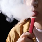 Young woman using electronic cigarette on black background, closeup